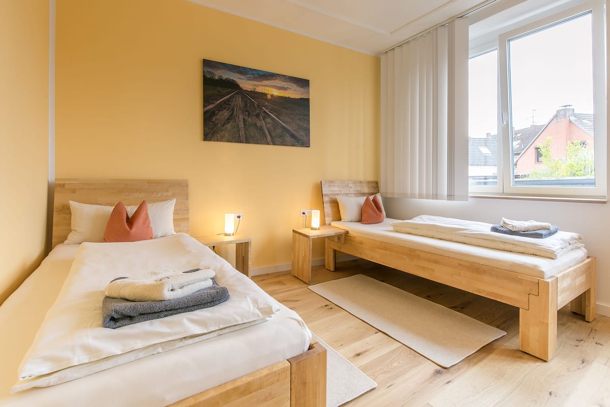 A bedroom with two beds, a bench, a painting, and a window with a view.