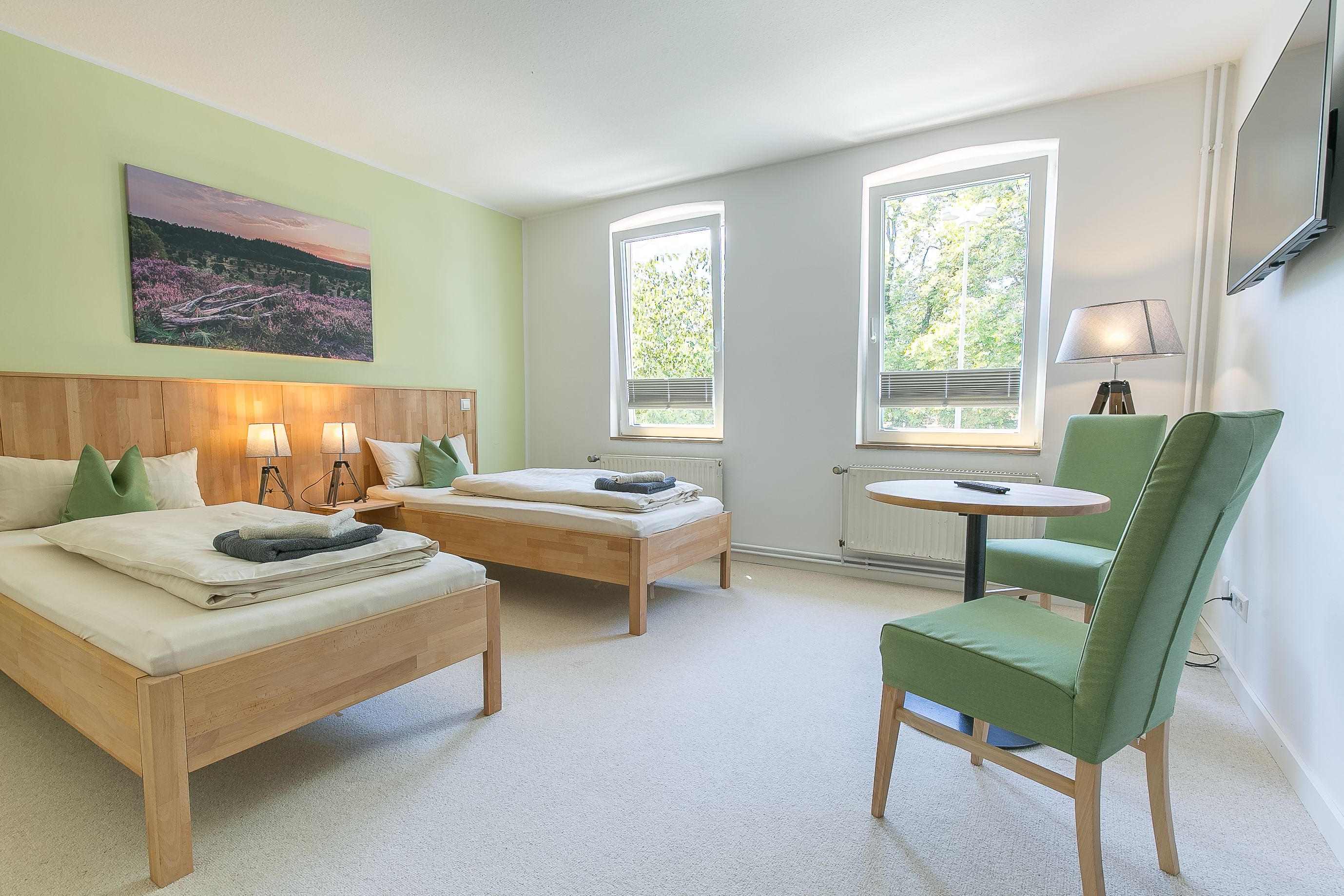 Ein Zimmer mit zwei Betten, einem grünen Sessel, einem kleinen Tisch und einem Bild an der Wand.
