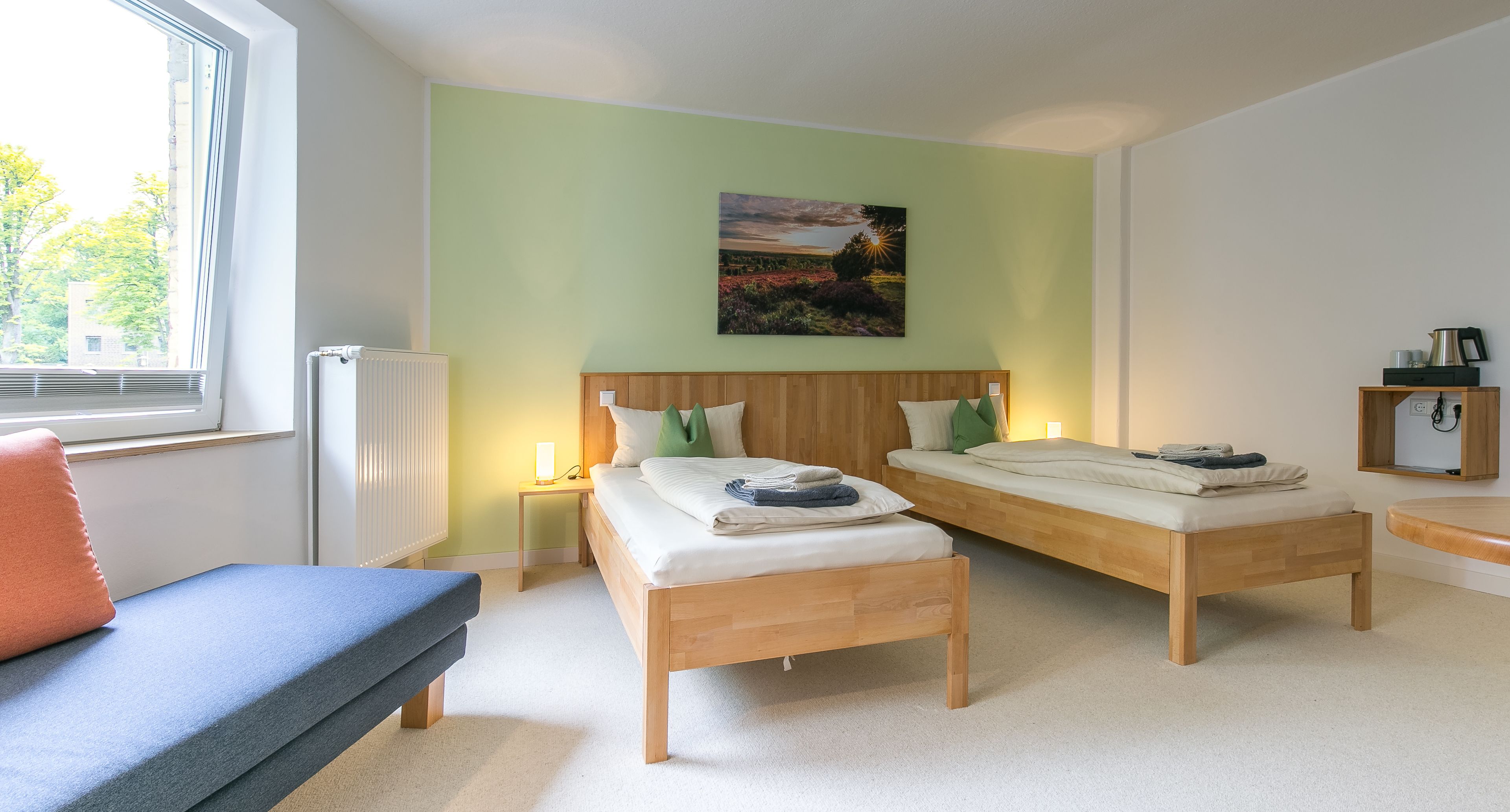 Ein Zimmer mit zwei Holzbetten, einer Bank, einem Heizkörper, einem Nachttisch und einem Gemälde an der Wand.