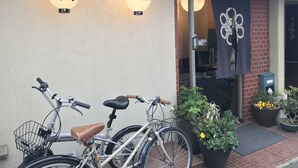 Entrada de un edificio con dos letreros iluminados, una bicicleta estacionada adelante y plantas en macetas.