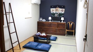 Una habitación tradicional japonesa con suelo de tatami, una mesa de madera baja con una bandeja de té, un escritorio con una computadora y una silla.