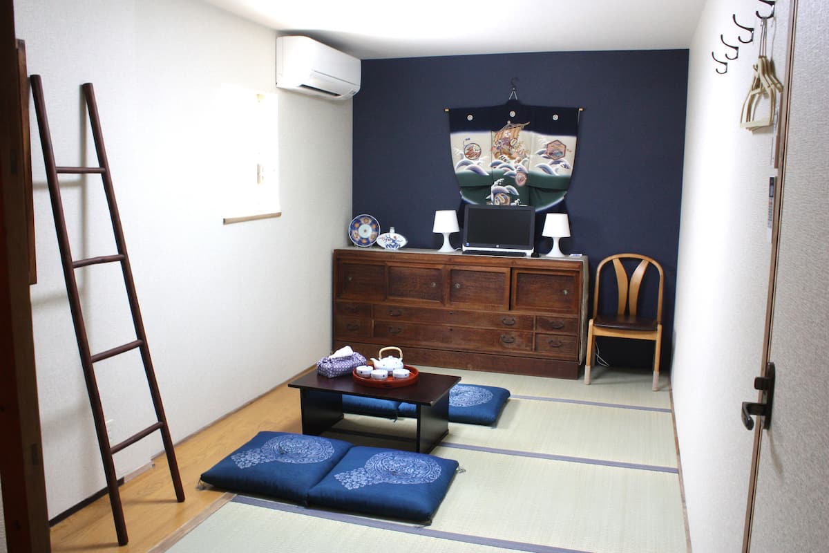 Una habitación tradicional japonesa con suelo de tatami, una mesa de madera baja con una bandeja de té, un escritorio con una computadora y una silla.