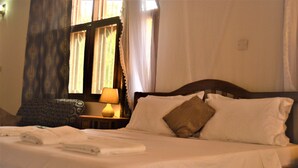 A neatly made bed with white linens, a bedside lamp, and a window with curtains. - PJ Lodge (Dar es Salaam)