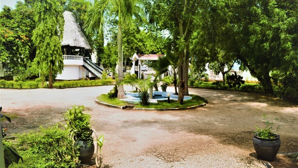 A courtyard with a thatched-roof structure, a central fountain, and surrounding greenery. - PJ Lodge (Dar es Salaam)