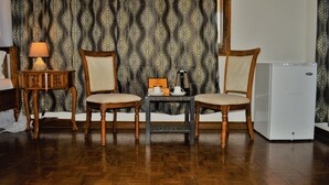 A room with two wooden chairs, a small table with a lamp, a refrigerator, and patterned curtains. - PJ Lodge (Dar es Salaam)