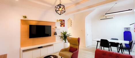 A modern living room with a flat-screen TV, a red sofa, a yellow armchair, and a small side table.