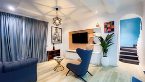 A modern living room with a sofa, a blue armchair, a small round table, and a TV mounted on the wall.