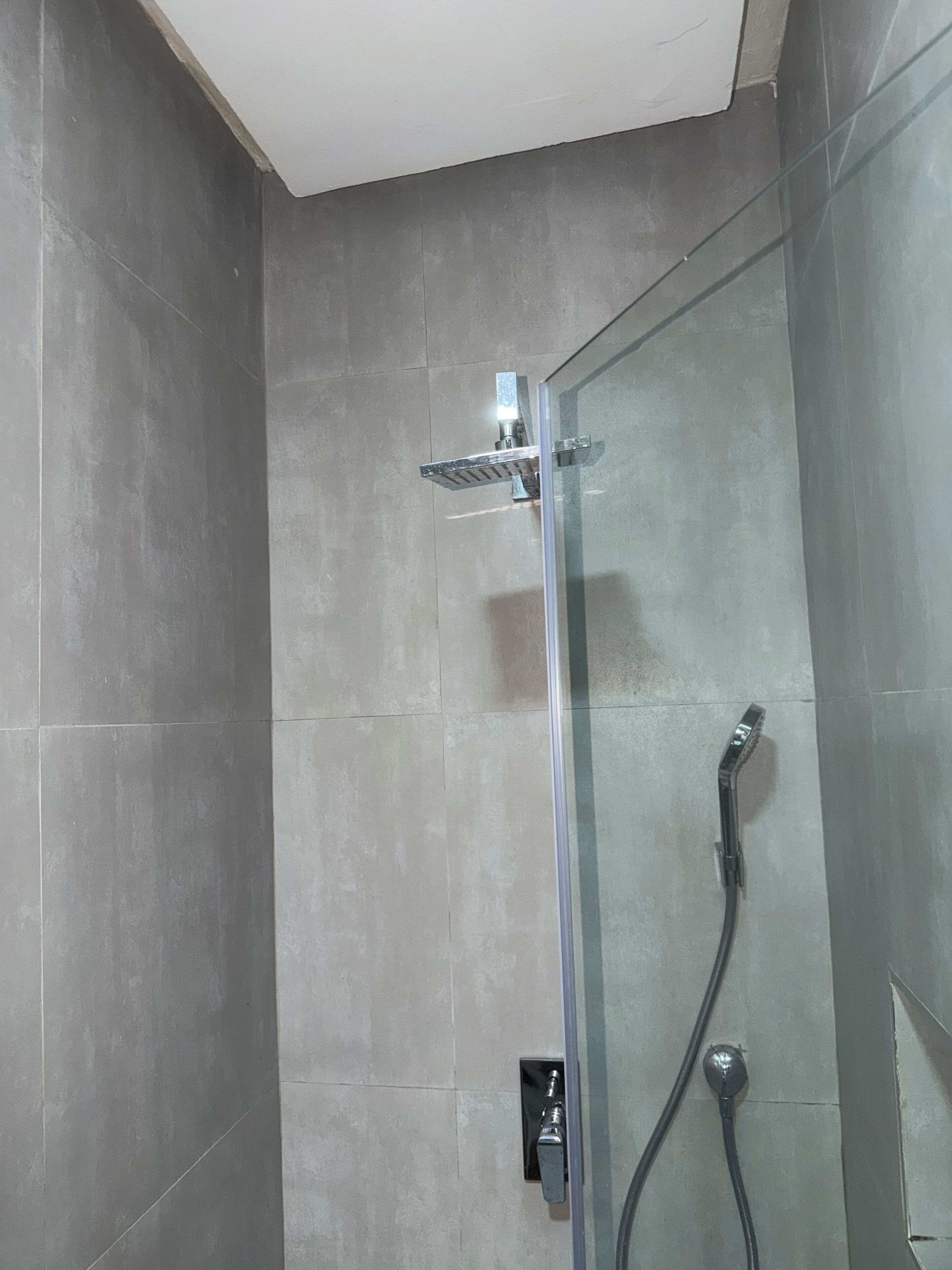 A glass-enclosed shower with a handheld showerhead and a wall-mounted faucet.