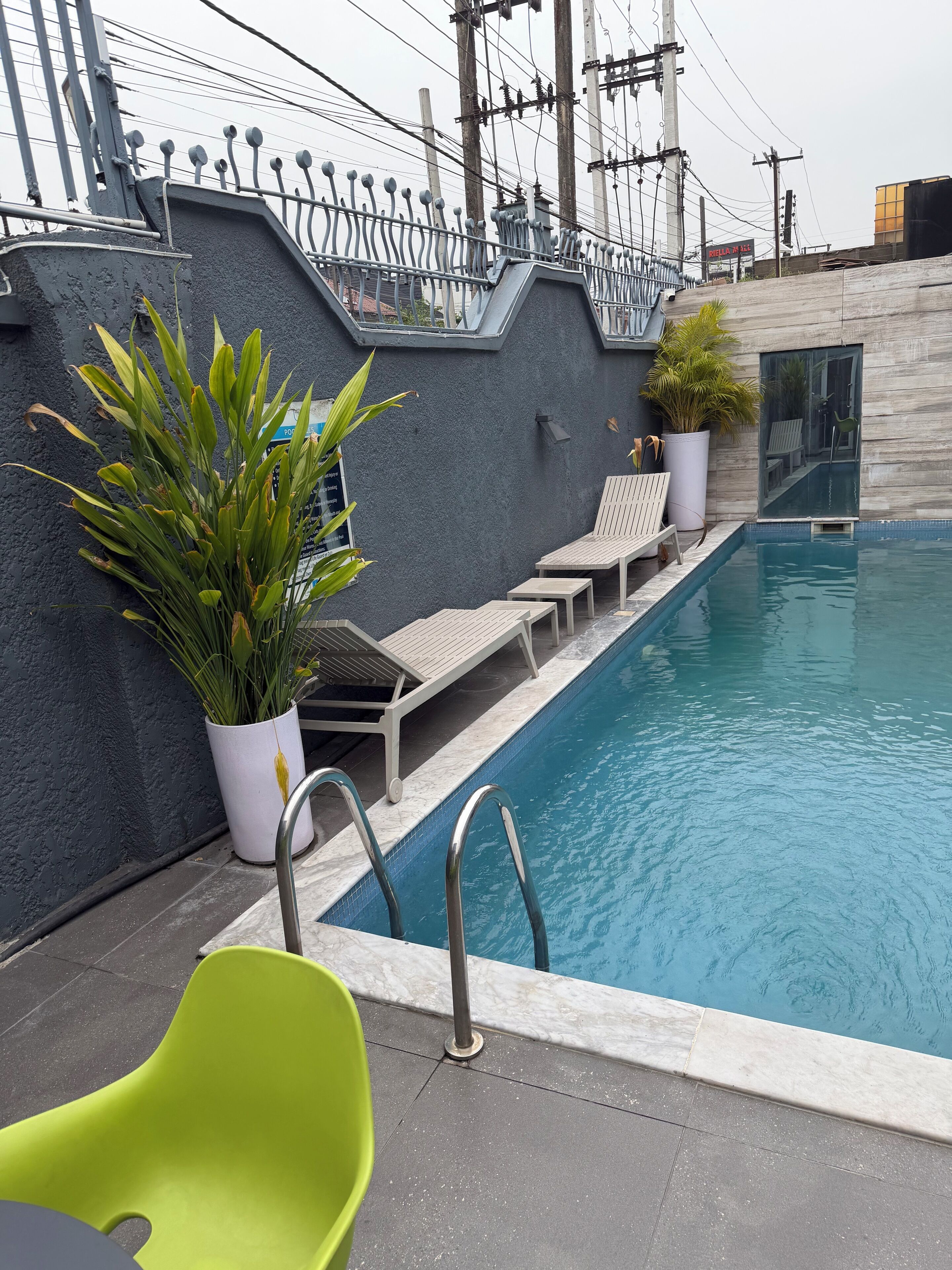 A pool area with lounge chairs, a green chair, and potted plants.