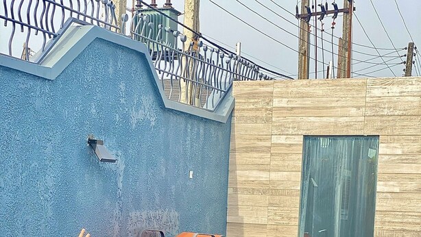 A swimming pool with a blue textured wall and a door. There are lounge chairs and a metal fence in the background.