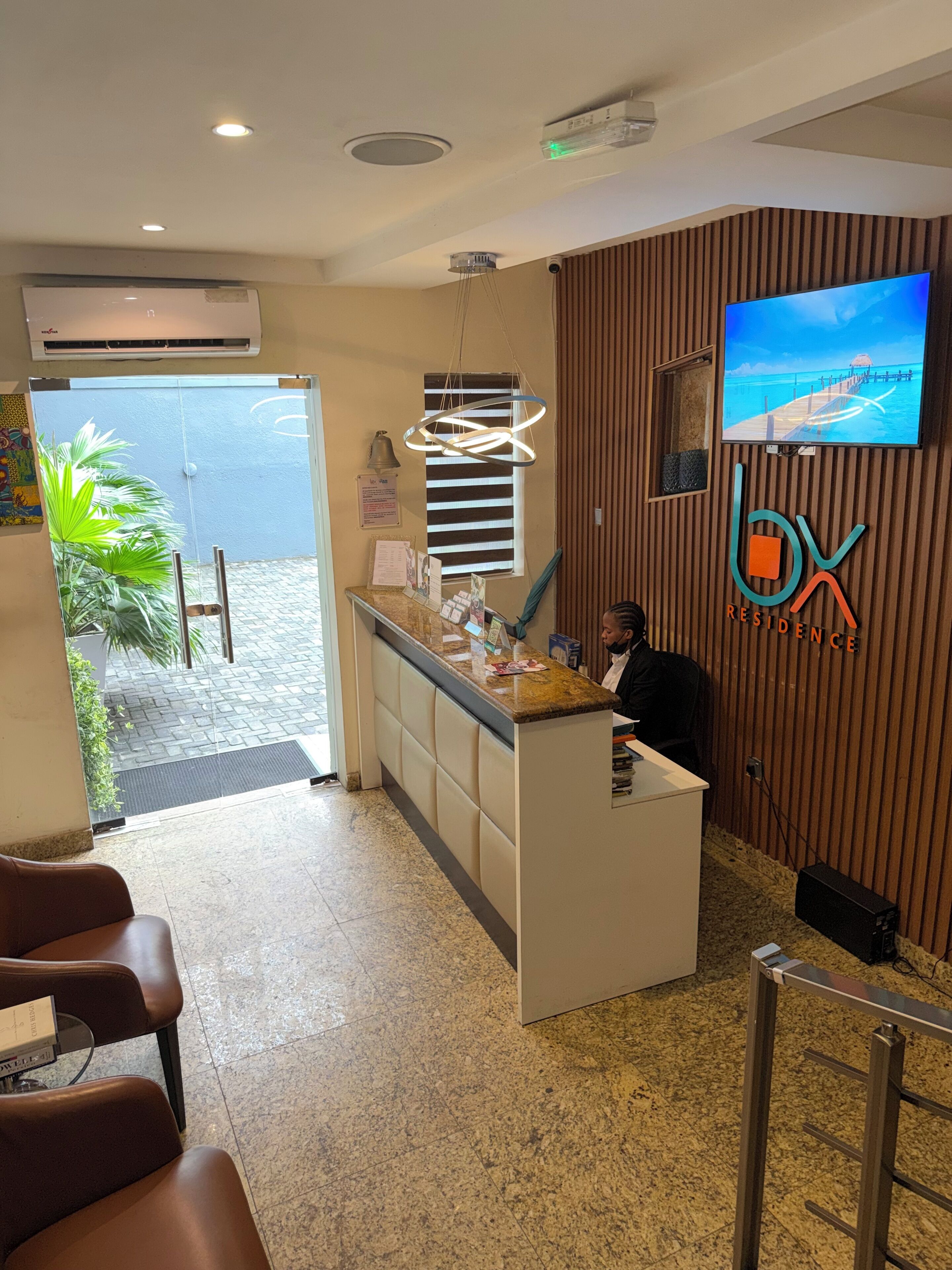 A reception area with a counter, a TV mounted on the wall, and a view of the outdoors through a glass door.