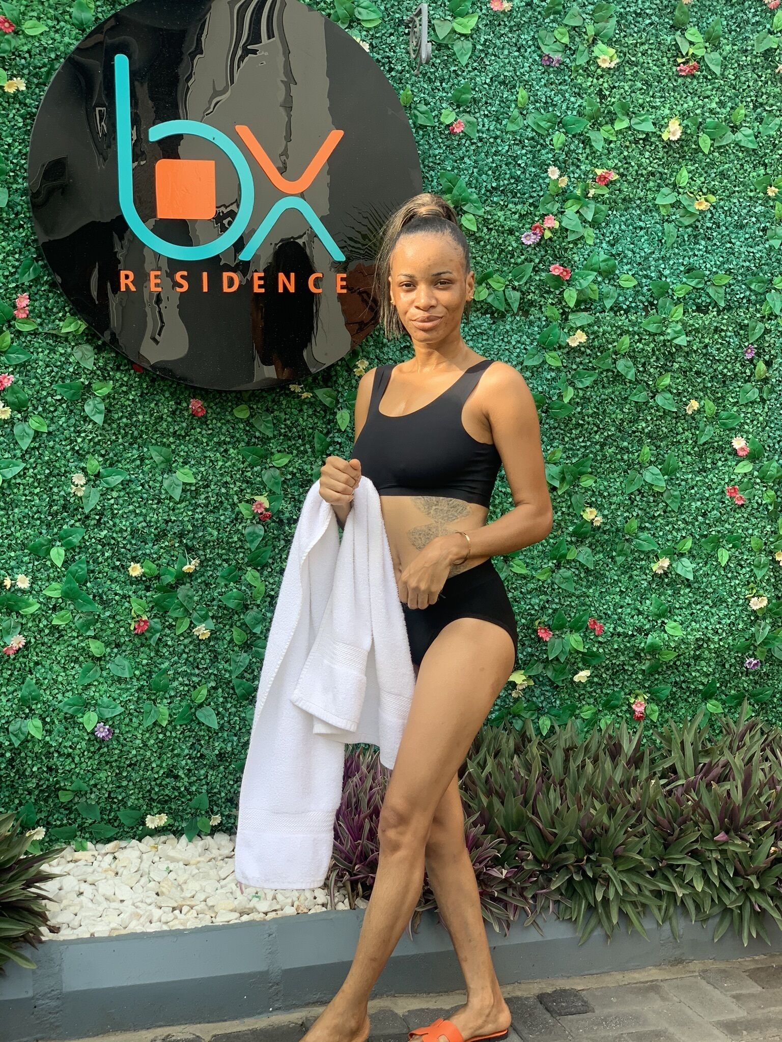 A woman standing in front of a wall with greenery and a sign that reads "box residence".