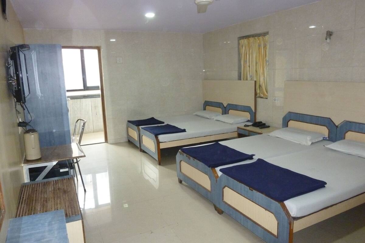 Habitación de hotel con tres camas individuales, un escritorio con silla, ventilador de techo y ventana con cortinas.