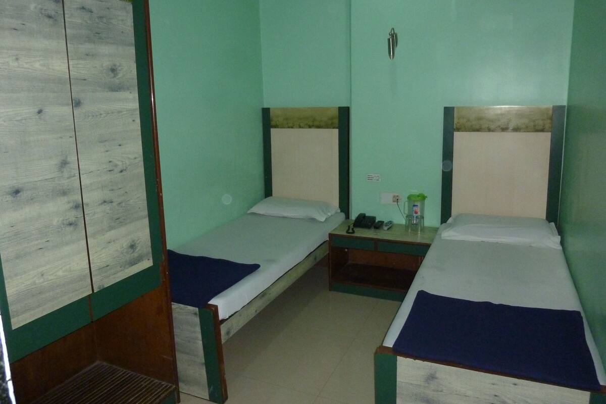 Una habitación con dos camas individuales, un armario de madera y una mesita con un teléfono y una botella de agua.