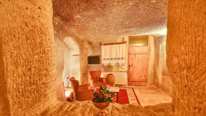 A cozy interior with a rustic stone wall, a wooden door, a red rug, and a wooden chair. - Mosaic Cave Hotel (Nevsehir)