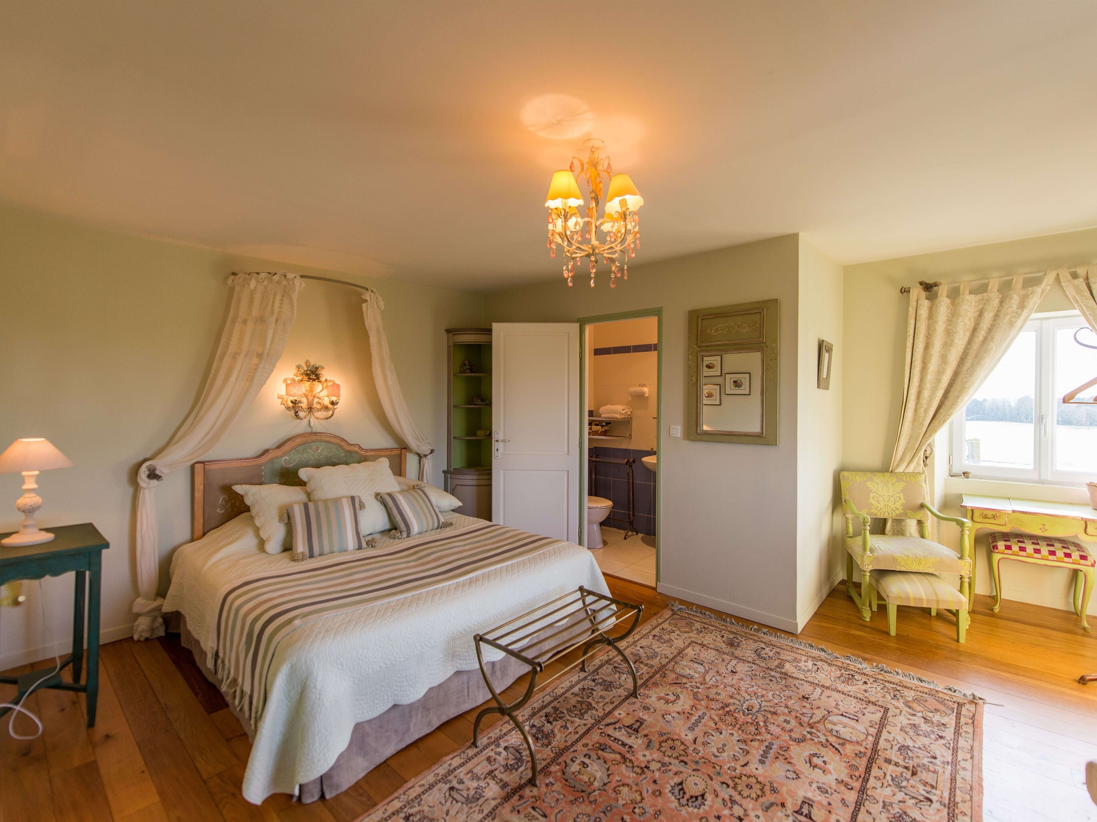 A bedroom with a canopy bed, bedside lamp, and a chandelier.