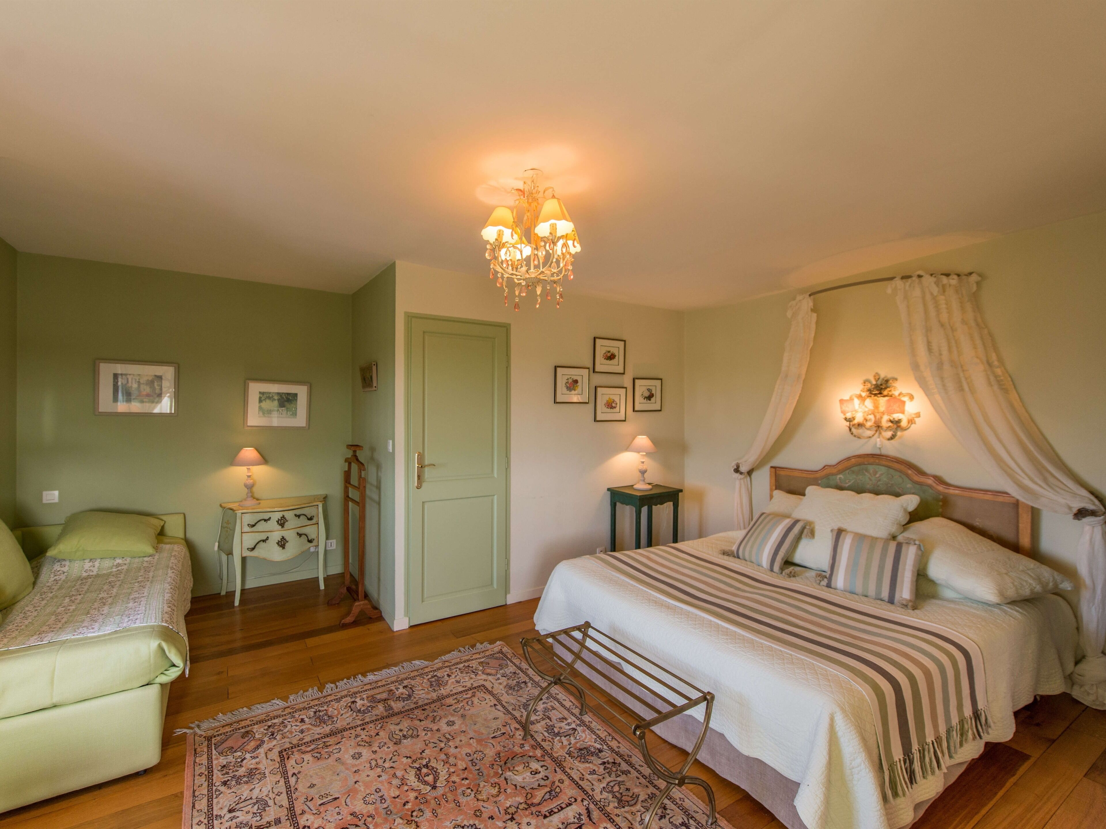 Quarto com cama, duas mesas de cabeceira, um criado-mudo, uma cadeira, um tapete e um candelabro.