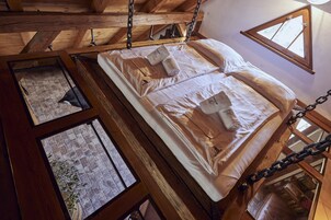 A loft-style bedroom with a wooden ceiling, a bed with white linens, and a view through a window.