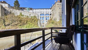A wooden deck with a chair overlooking a river and a historic building with arched windows. - Krumlov Mill Apartments (Cesky Krumlov)