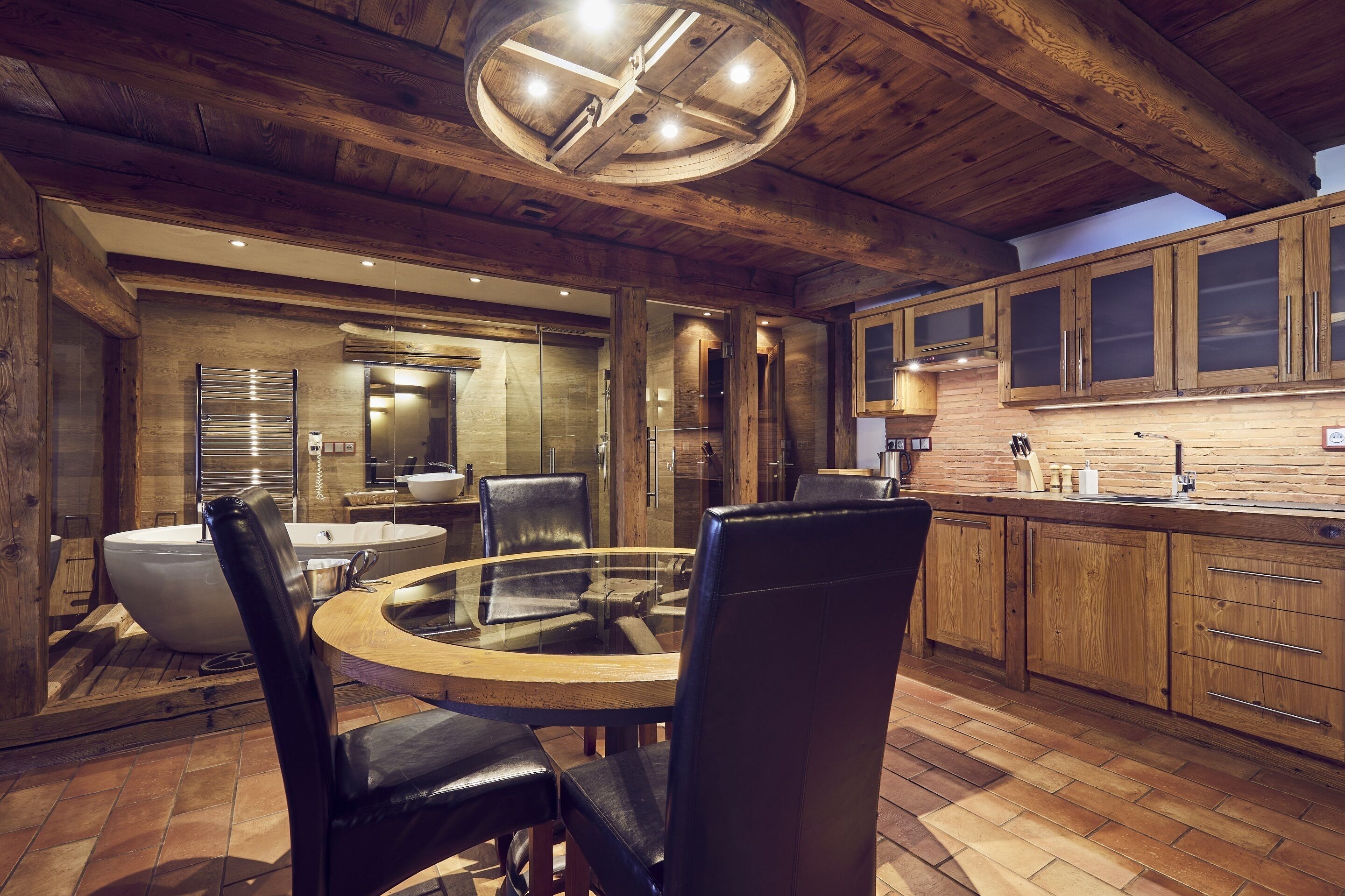 A rustic kitchen with wooden cabinets, a round dining table, and a large window.