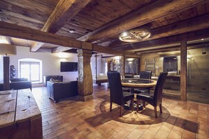 Una habitación amplia con techo de madera, una mesa redonda de comedor con sillas, un sofá y una zona de cocina con refrigerador y lavaplatos.