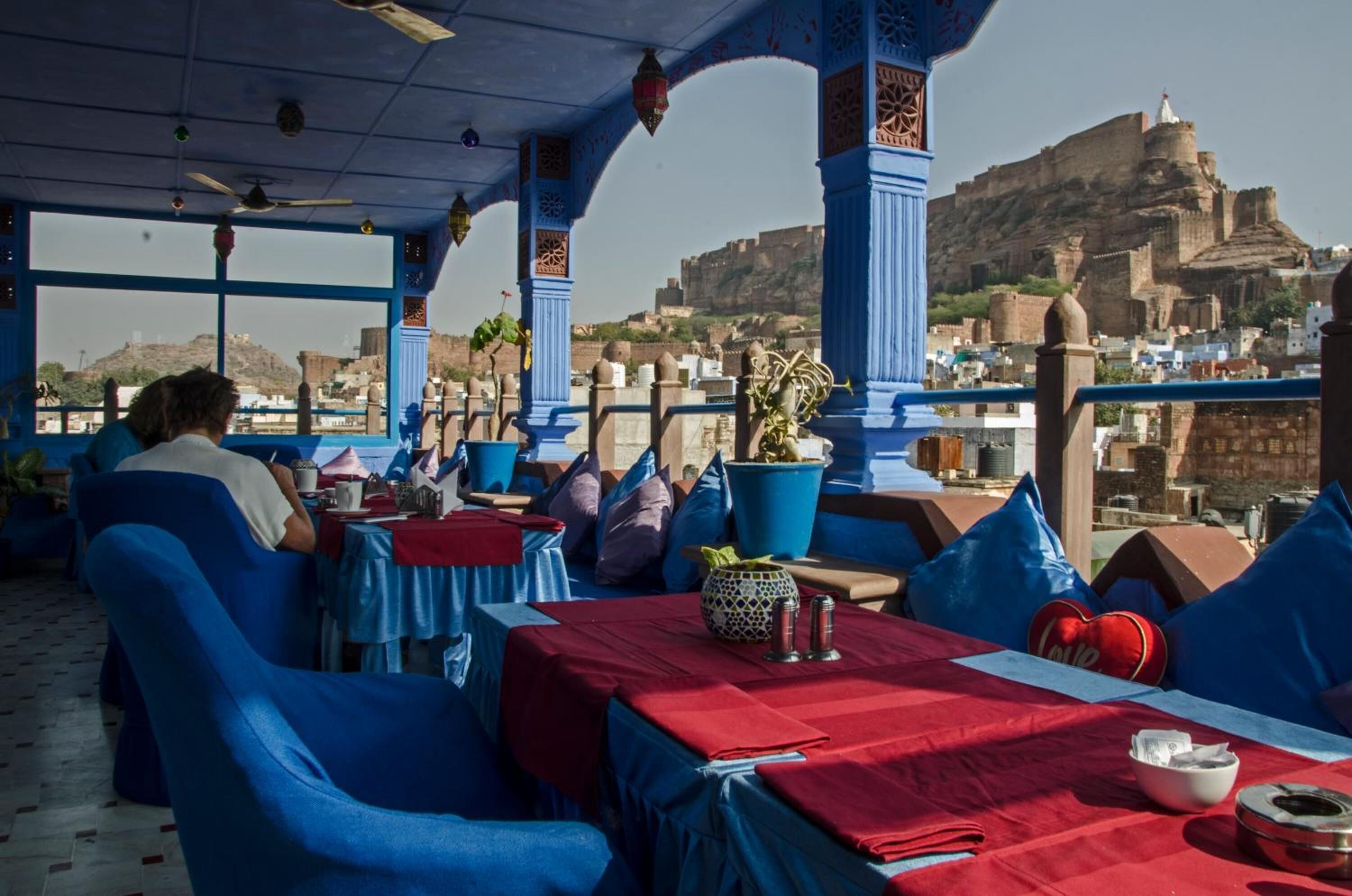 A restaurant with blue furniture and red tablecloths, overlooking a historic fort.