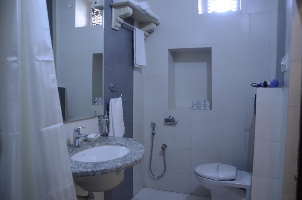 Et badeværelse med vask, spejl, håndklædestang, bruser og toilet.
