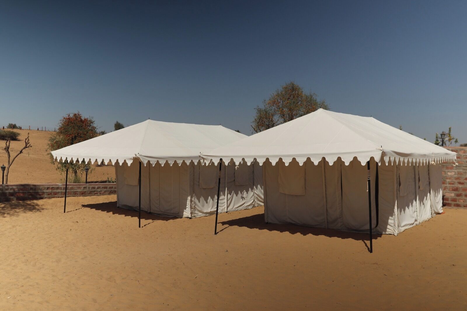 Two white tents with a scalloped edge, set in a desert environment with a clear sky.
