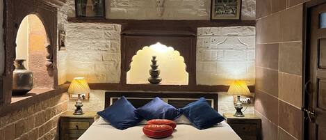 A bedroom with a bed, two bedside lamps, a ceiling fan, and a decorative wall with a window.