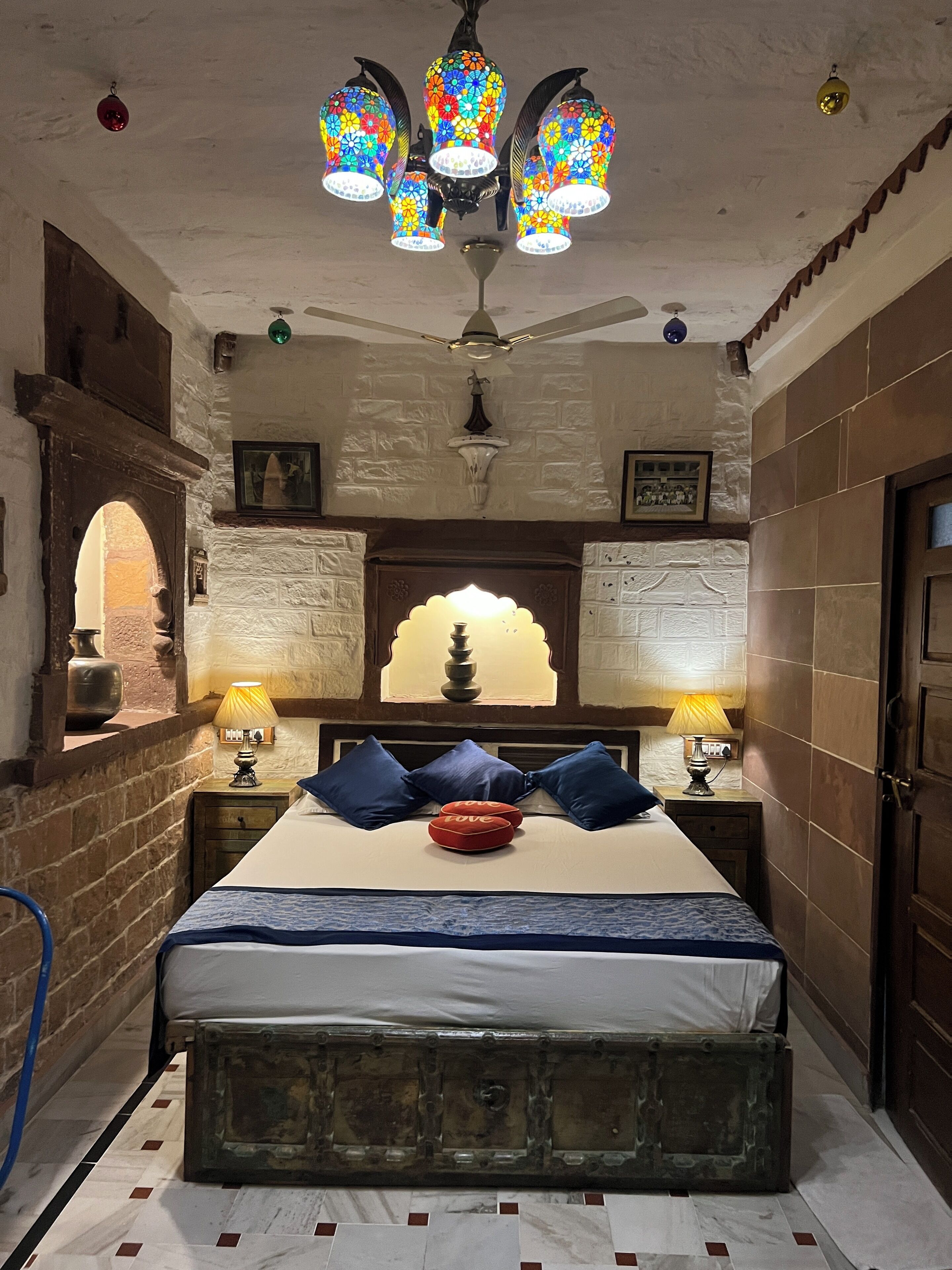 Une chambre à coucher avec un lit, un lustre, un ventilateur de plafond et un mur en briques.