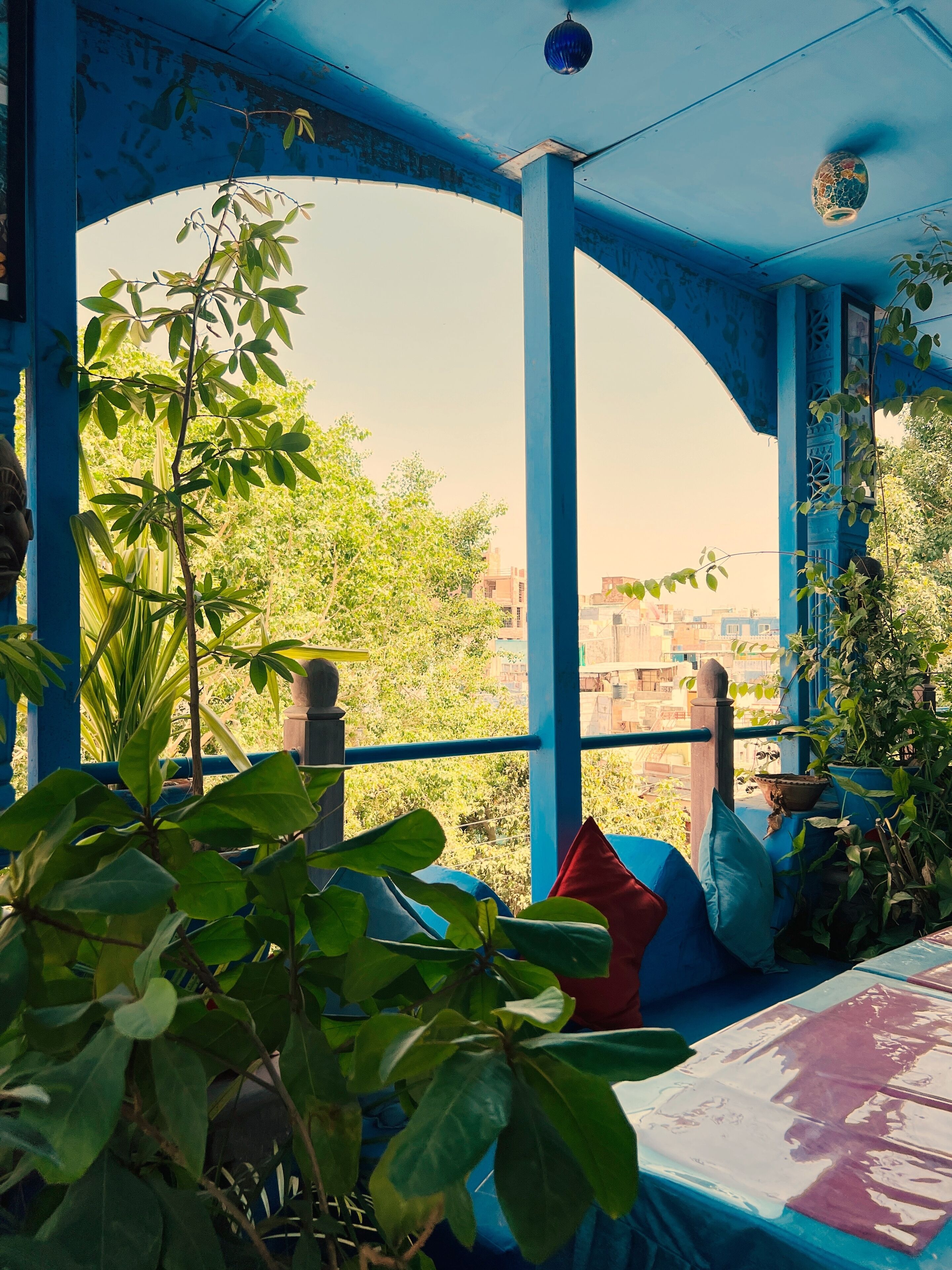 A room with a blue ceiling and walls, a bed with a patterned bedspread, and a view of greenery and buildings outside.