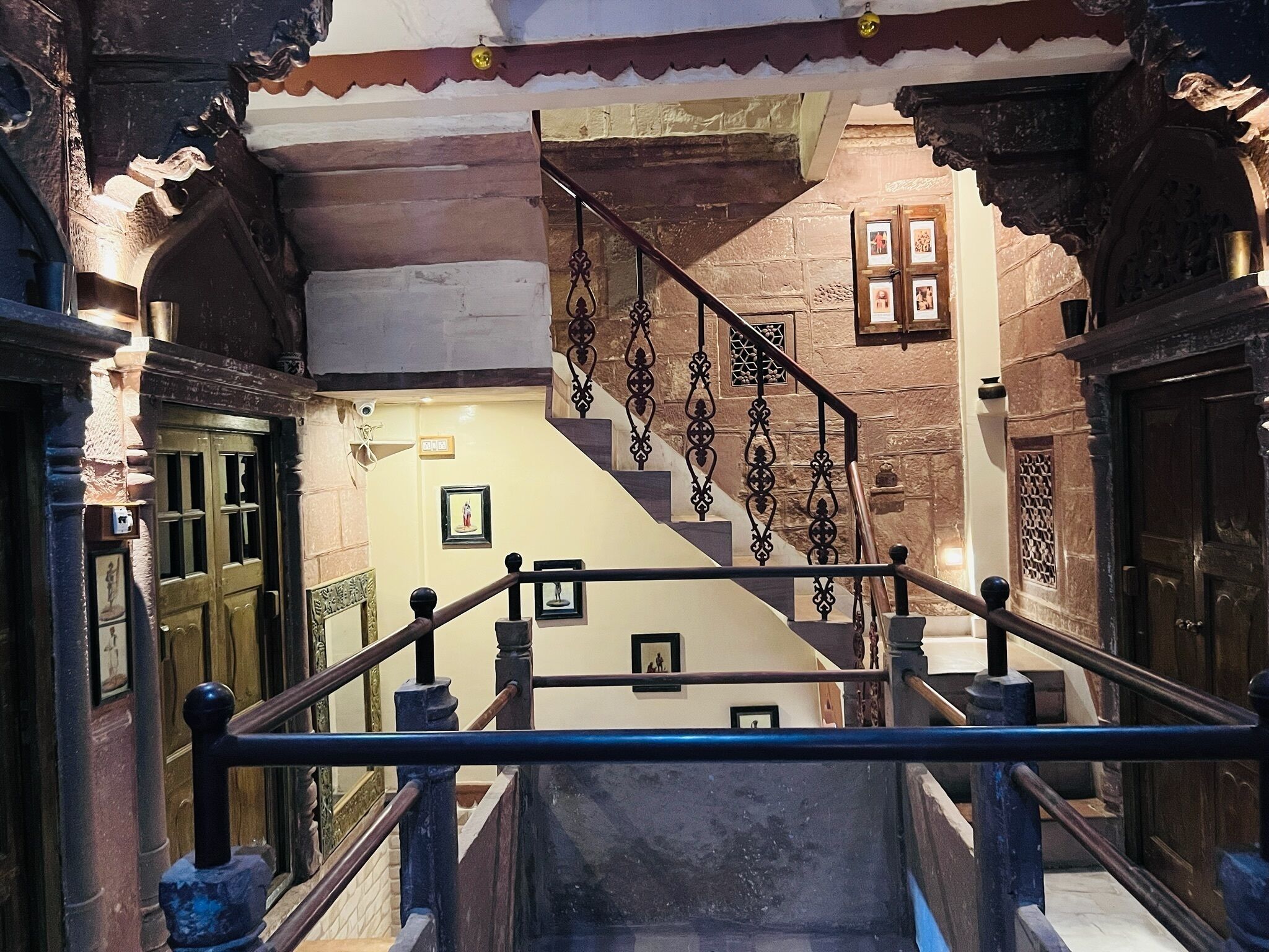 Una escalera con barandillas decoradas y paredes de piedra, que conduce a una puerta con un panel de vidrio.