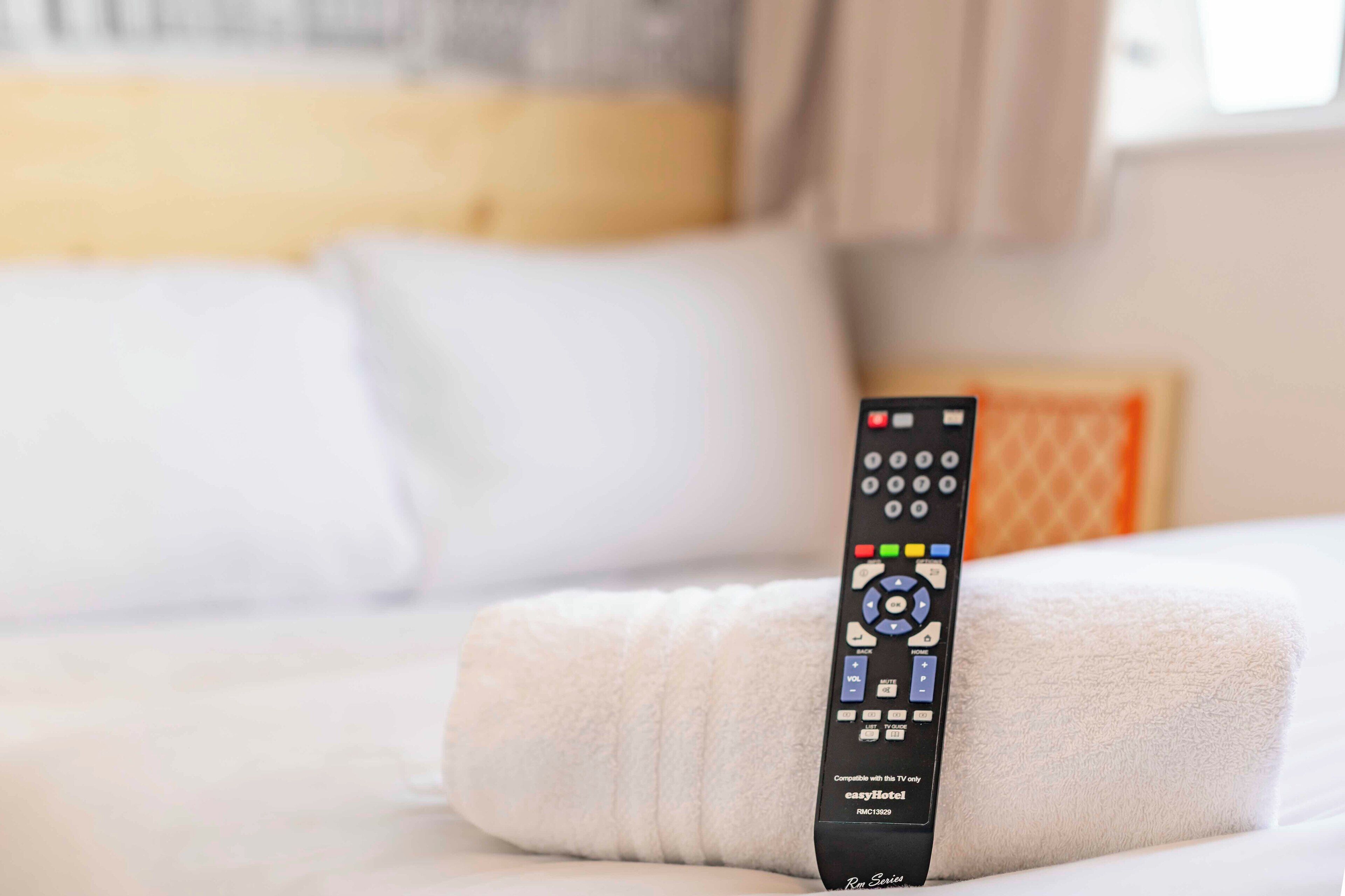 Un control remoto sobre una cama bien hecha con sábanas blancas.