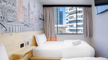 Quarto de hotel com uma janela grande, uma cama, uma escrivaninha e um mural na parede.