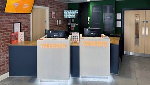Een hotel receptie met twee balies, een televisiescherm en een 'WELCOME' bord.