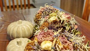 A dining table with a centerpiece of dried flowers and a pumpkin.