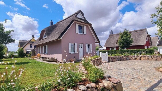 A traditional house with a steep gabled roof, a well-maintained garden with flowering plants, and a stone pathway leading to the entrance.