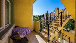 Un balcone con tavolo e sedia, una scala e vista su edifici sullo sfondo.