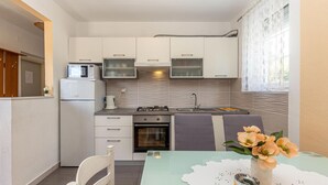 Una cucina funzionale con mobili bianchi, un forno a microonde integrato, un piano cottura a gas e un lavello. C'è un piccolo forno e un tavolo con una sedia.