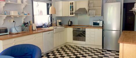Une cuisine de taille réduite avec des meubles blancs, un carrelage noir et blanc, un four à micro-ondes, un réfrigérateur et une chaise bleue.