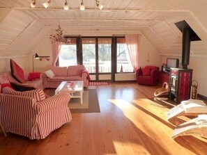 Acogedor dormitorio en el ático con muebles a rayas, chimenea y ventanas amplias.