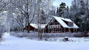 A cabin with a sloped roof, surrounded by snow-covered trees and a snow-covered ground.