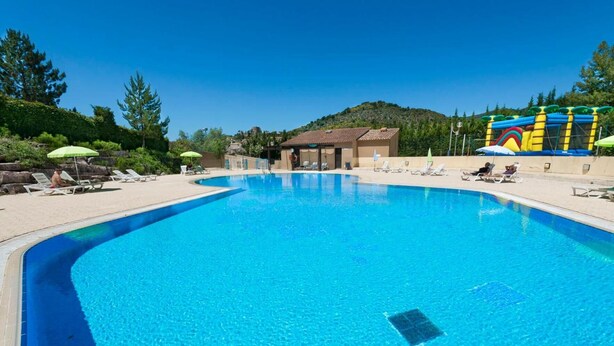 A clear blue swimming pool with lounge chairs and umbrellas, surrounded by greenery and a building in the background. - Village vacances Léo Lagrange Montbrun (Montbrun-les-Bains)