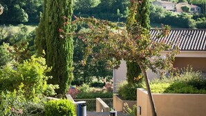 A landscaped garden with tall cypress trees, a pathway, and a building with a tiled roof. - Village vacances Léo Lagrange Montbrun (Montbrun-les-Bains)