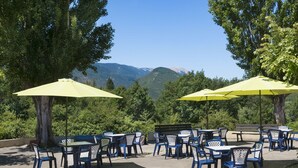 An outdoor seating area with tables and chairs, yellow umbrellas, and a view of mountains. - Village vacances Léo Lagrange Montbrun (Montbrun-les-Bains)