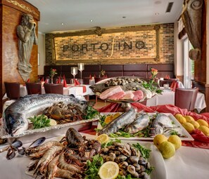 A seafood buffet with various fish and shellfish, a brick wall with 'PORTOFINO' signage, and a statue.