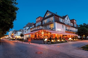 A hotel with a restaurant on the ground floor, featuring a cobblestone street and a clear evening sky.