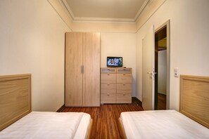 Habitación de hotel con dos camas, un armario de madera, un televisor y una puerta que da a un vestidor.