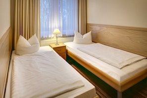 Ett hotellrum med två separata sängar, ett nattduksbord med en lampa och ett fönster med gardiner.