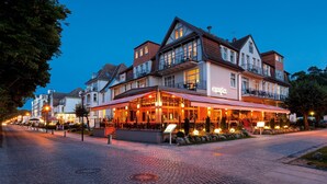 Hotel met restaurant op de begane grond, met een geplaveid straatje en heldere avondlucht.